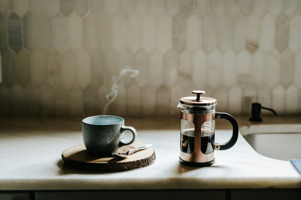 Steaming cup of coffee beside a French press on a kitchen counter