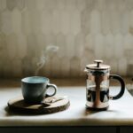 Steaming cup of coffee beside a French press on a kitchen counter