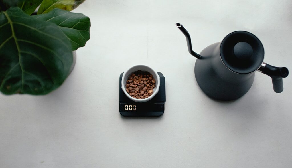 Top view of coffee beans on a scale beside a black gooseneck kettle