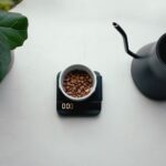 Top view of coffee beans on a scale beside a black gooseneck kettle