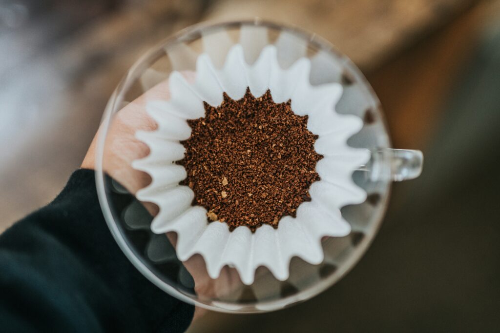 Hand holding a pour-over dripper with coffee grounds in a paper filter