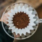 Hand holding a pour-over dripper with coffee grounds in a paper filter