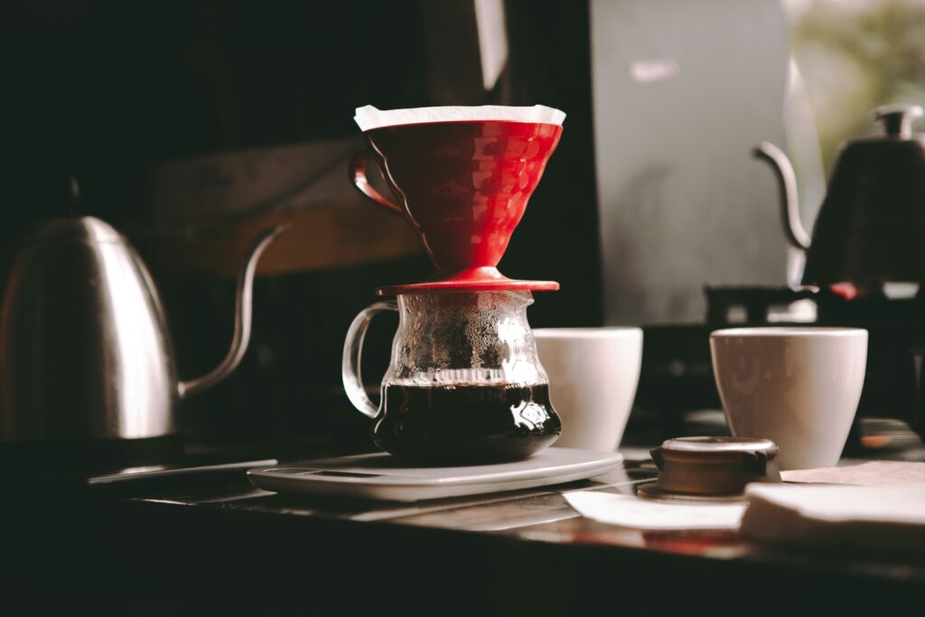 Pour-over coffee setup with a red dripper, glass server, kettle and cups
