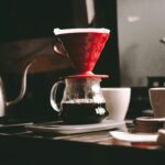 Pour-over coffee setup with a red dripper, glass server, kettle and cups