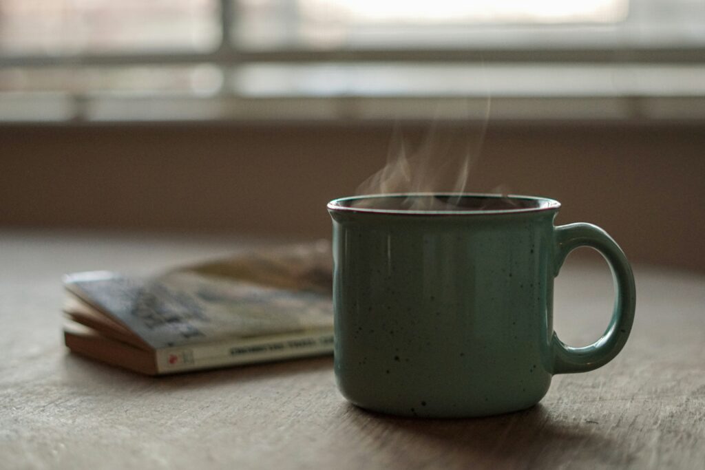 Steaming green mug of coffee on a table next to a book